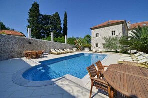 A swimming pool with lounge chairs and a wooden table, surrounded by a stone wall and a building with a tiled roof. - Stone House Seafront Villa (Kotor)