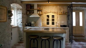 Una cocina con pared de piedra, una isla de madera con taburetes, horno empotrado y ventana con cortinas.