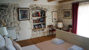 Un dormitorio con pared de piedra, una estantería, una cama con toallas ordenadas y una ventana con cortinas rojas.