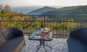 A balcony with a table set for two, featuring a bottle of wine, glasses, bread, and cured meat. - Villa Zoranna with Pool (Budva)