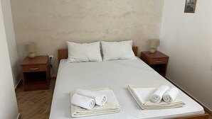 Ein ordentlich bezogenes Bett mit weißen Leinen und zwei aufgerollten Handtüchern. Zwei Nachttische mit Lampen und einer kleinen Schublade sind vorhanden.