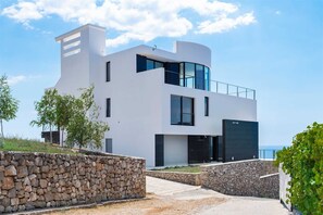 A modern two-story building with a flat roof, large windows, and a stone retaining wall.