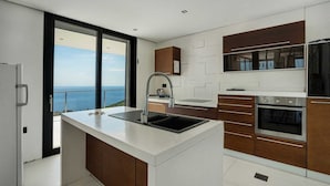 Una cocina moderna con una isla grande, electrodomésticos de acero inoxidable y vista al mar.