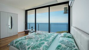 Un dormitorio moderno con una cama grande, una mesita pequeña y vistas al mar.
