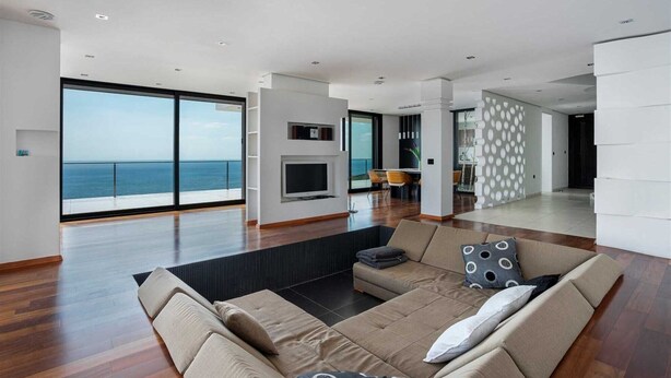Una sala de estar moderna con un sofá grande, un televisor de pantalla plana y vista al mar.
