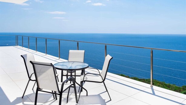 En terrasse med bord og stole, med udsigt over et klart, blåt hav.