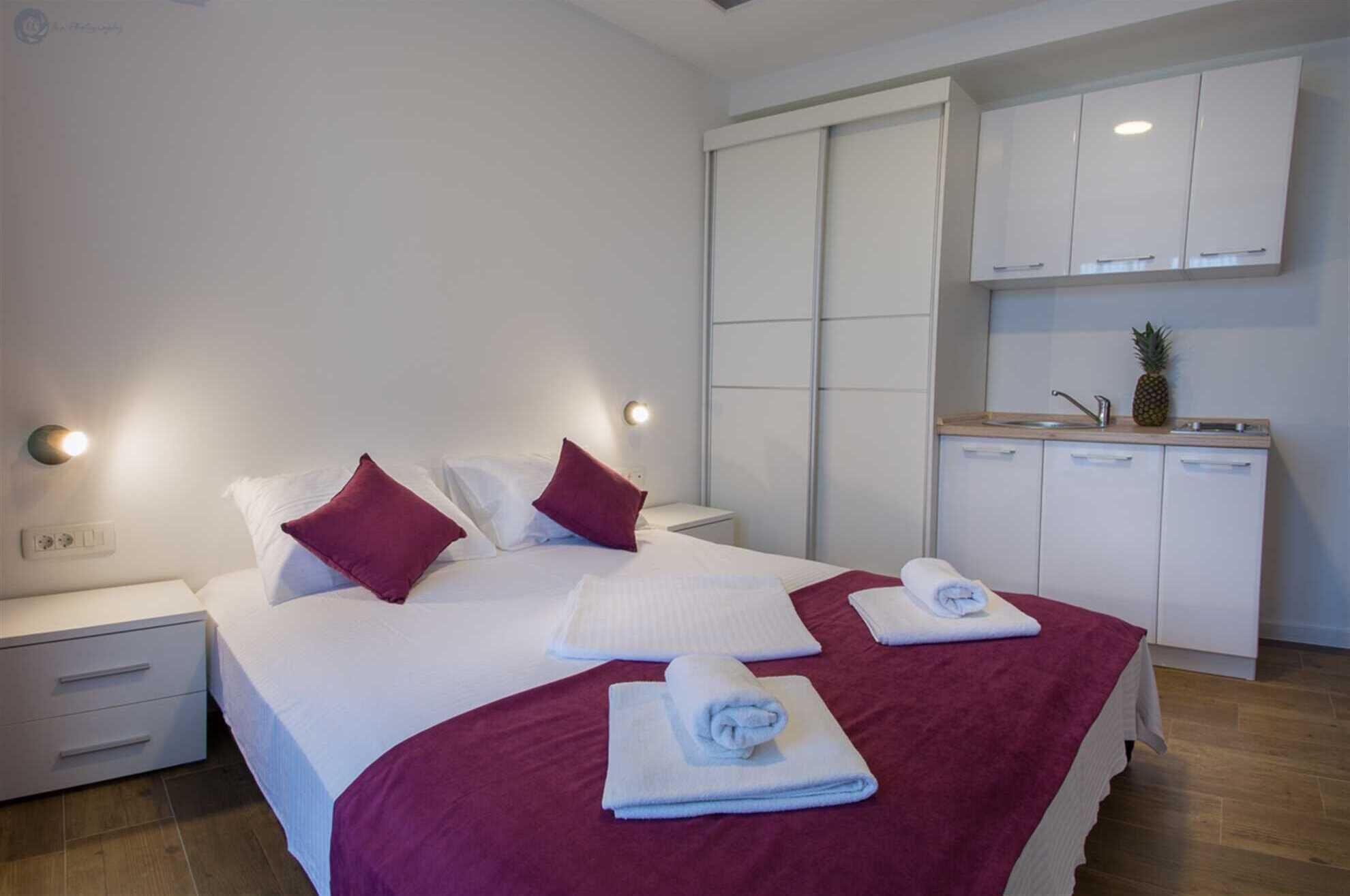 A hotel room with a bed, two nightstands, a wardrobe, and a kitchenette.