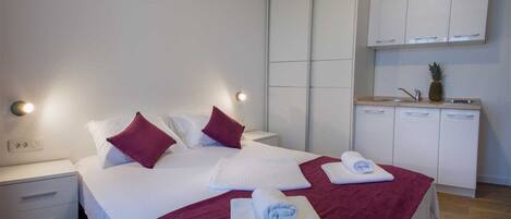 A hotel room with a bed, two nightstands, a wardrobe, and a kitchenette.