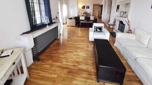 A spacious living room with a wooden floor, white sofas, a black coffee table, and a fireplace. - Villa Rustica Mediteranea (Budva)