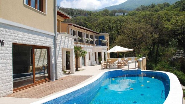 A modern villa with a swimming pool, a wooden deck, and a view of a mountainous landscape. - Villa Rustica Mediteranea (Budva)
