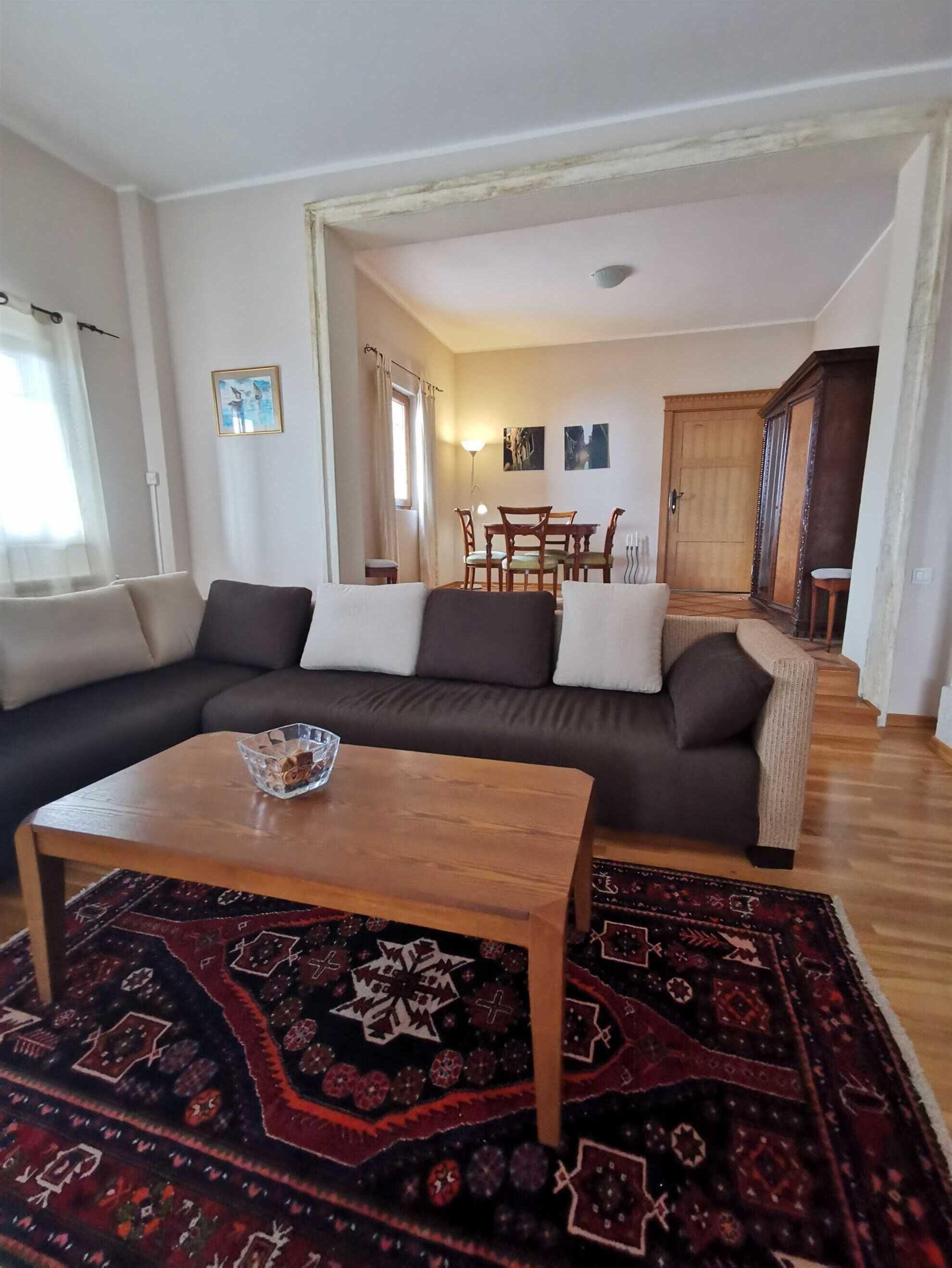 Una sala de estar con un sofá marrón oscuro, una mesa de centro de madera y una alfombra estampada.