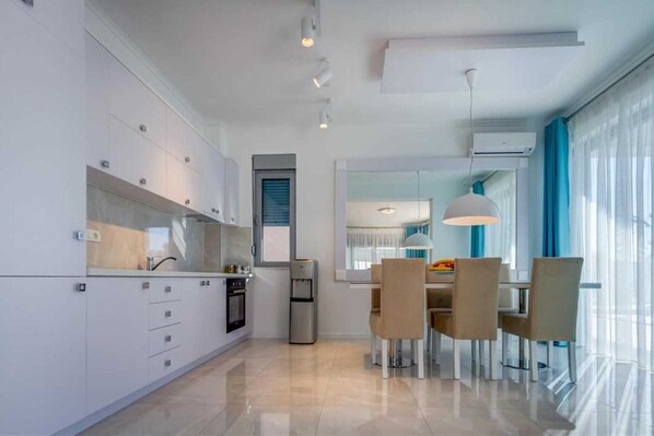 Une cuisine moderne avec des meubles blancs, un four encastré et un coin repas comprenant une table et des chaises.