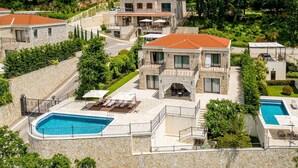 A two-story stone building with a swimming pool, outdoor seating, and a landscaped garden. - Oak Leaf Residence Villa 1 (Budva)