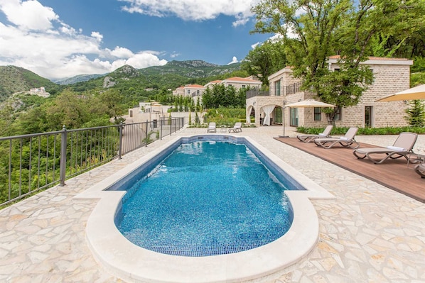 A swimming pool with a stone deck, surrounded by lounge chairs and a view of green hills.