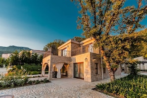 A two-story stone house with a balcony, arched doorways, and a stone pathway leading to the entrance.