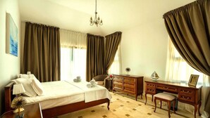 A hotel room with a bed, a desk, a chair, a dresser, and a chandelier. - Oak Leaf Residence Villa 1 (Budva)