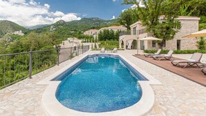 Piscina com borda de pedra, rodeada por espreguiçadeiras e um deck de pedra.