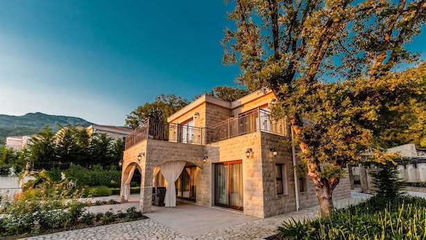 A two-story stone building with a balcony, arched doorways, and a stone pathway leading to the entrance.