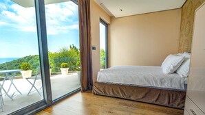 Un dormitorio con un gran ventanal corredera que da a un balcón con plantas en macetas y vistas a la vegetación.