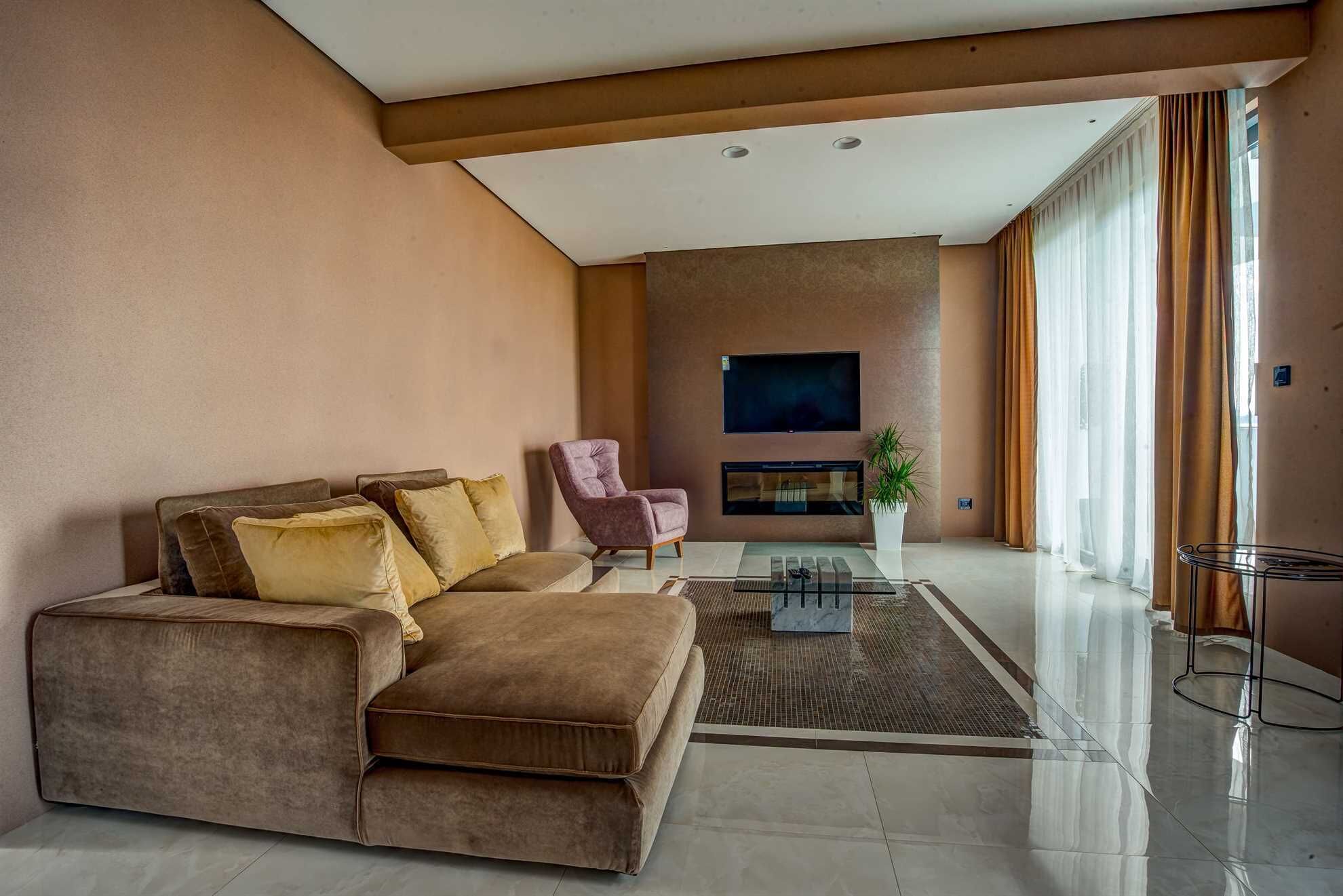 A modern living room with a sectional sofa, a pink armchair, a flat-screen TV, and a fireplace.