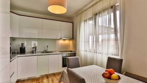 Een moderne keuken met witte kasten, een spoelbak en een fornuis. Er staat een eettafel met een fruitschaal en twee stoelen.
