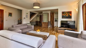 Een woonkamer met grijze banken, een salontafel met fruit, een televisie en een trap naar een andere kamer.