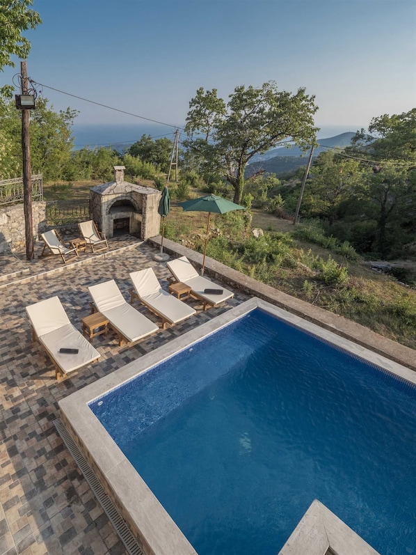 A pool area with lounge chairs and a stone fireplace.