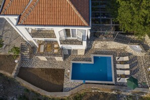 An aerial view of a house with a swimming pool, a balcony, and a garden area.