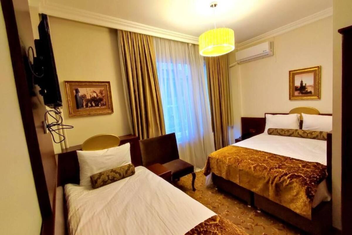 Una camera d'albergo con due letti, una scrivania, una sedia, una lampada e un quadro appeso al muro.