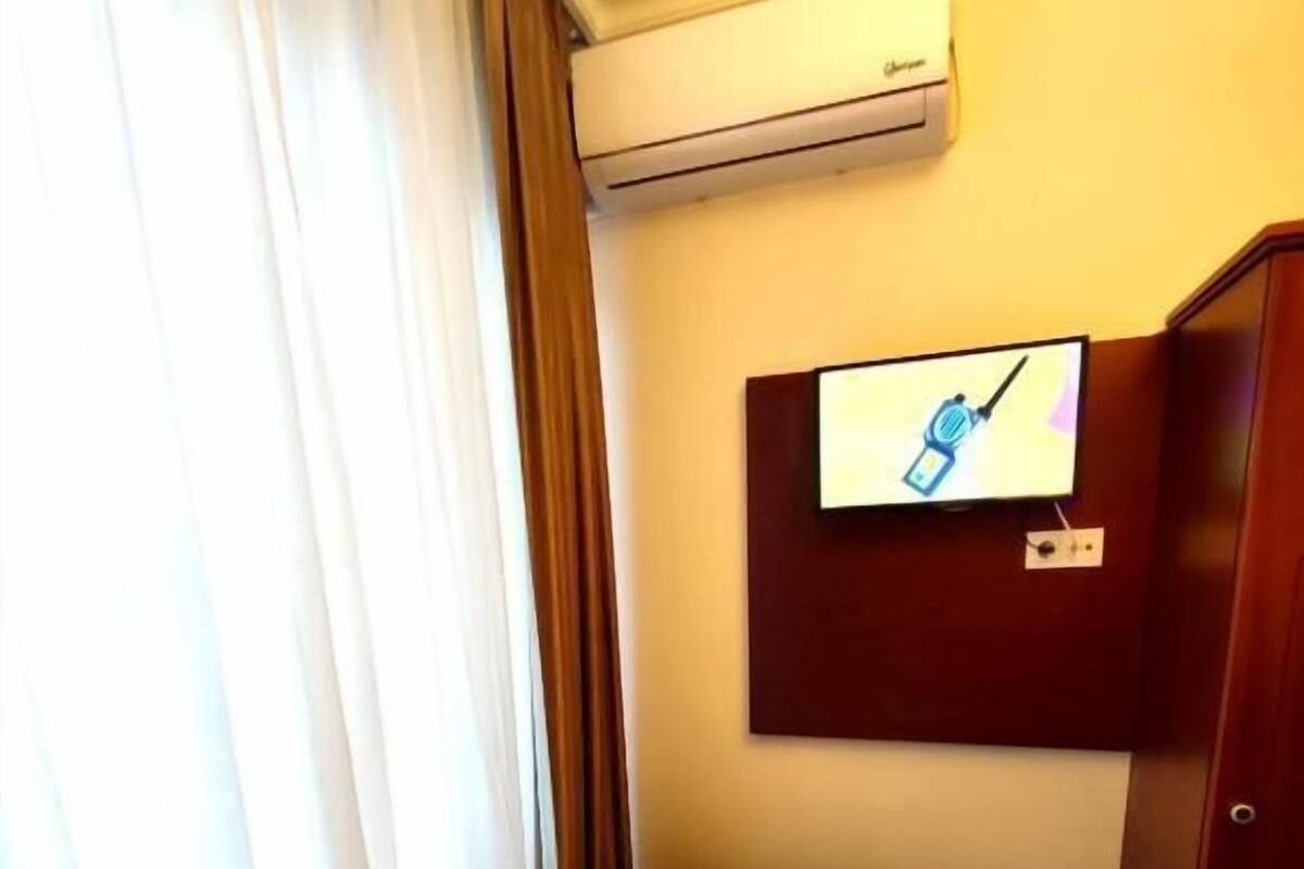 Una camera d'albergo con un letto, tende, un condizionatore d'aria, un televisore a parete e un armadio in legno.