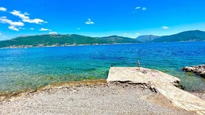 On peut clairement voir une plage de galets qui s’étend jusqu’à une mer calme, avec des montagnes en arrière-plan.
