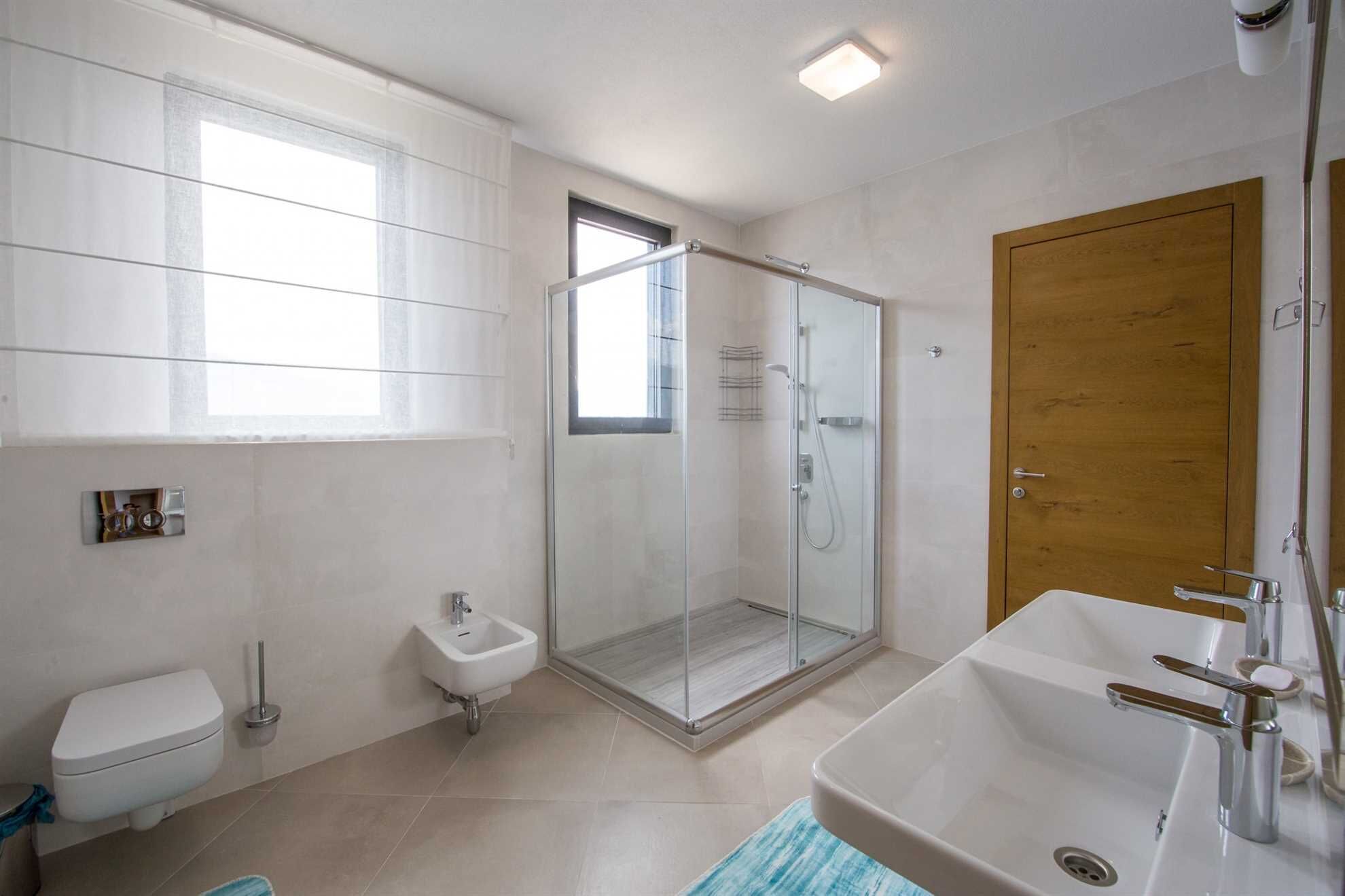A modern bathroom with a glass-enclosed shower, a wooden door, a large sink, and a toilet.