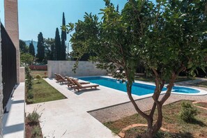 Piscina com espreguiçadeiras, cercada por um jardim e um edif ício.