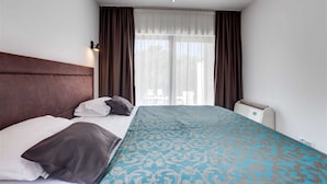 Ein Hotelzimmer mit einem großen Bett, einem Nachttisch, einem Fenster mit Vorhängen und einer Deckenleuchte.