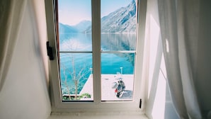 Et vindue med udsigt til en sø og bjerge, en scooter parkeret udenfor, samt en dør med håndtag.