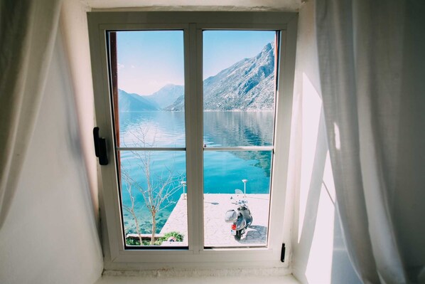 A window with a view of a lake and mountains, a scooter parked outside, and a door with a handle.