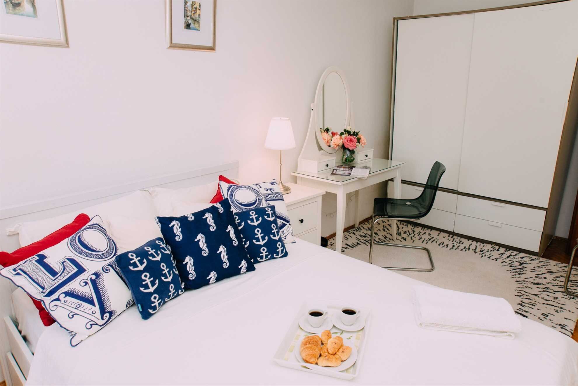 Une chambre d’hôtel équipée d’un lit, d’un bureau, d’une chaise, d’un miroir et d’un plateau avec des pâtisseries et du café.