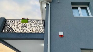 Um edifício moderno com fachada cinzenta, varanda com grades de metal preto elaboradas e uma pequena luz vermelha na parede.