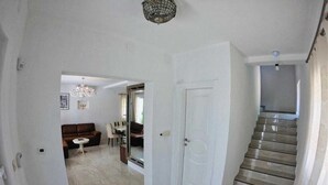 Um corredor espaçoso com escadas que levam a um segundo andar, uma sala de jantar com lustre e um espelho grande refletindo o ambiente.
