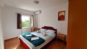 A bedroom with a bed, a window with curtains, a radiator, a wall-mounted air conditioner, a nightstand, and a painting. - Villa Charming Vineyard (Budva)