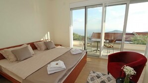 Een slaapkamer met een groot bed, een rode stoel, een klein tafeltje met een vaas, en een balkon met een tafel en stoelen.