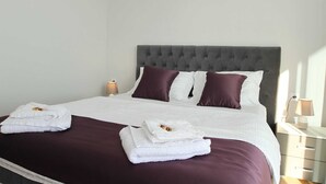 Een net opgemaakt bed met witte en bordeauxrode beddengoed, twee kussens en twee opgevouwen handdoeken op het bed.