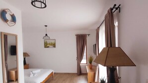 Un dormitorio amplio con piso de madera, una cama, un escritorio con lámpara, un espejo y un cuadro en la pared.