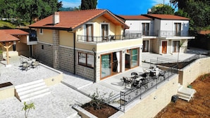Una casa de dos pisos con un balcón, un patio con mobiliario exterior y fachada de piedra.
