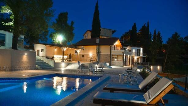 Una casa de dos pisos con piscina, mobiliario exterior y un patio bien iluminado.
