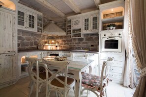 Une cuisine rustique avec des murs en pierre, des meubles blancs et un four d’époque.