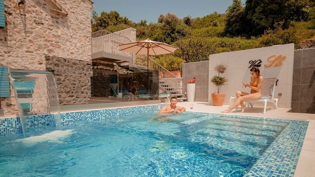 A swimming pool with clear blue water, a stone wall, and a modern building with a balcony. - Villa Stella Adriatica (Tivat)