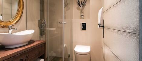 Un bany amb un tocador de fusta, un lavabo blanc, un compartiment de dutxa de vidre i un vàter.