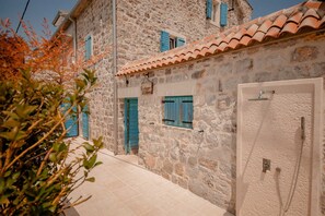 Un bâtiment en pierre avec des volets bleus, un toit en tuiles et une porte équipée d’un pommeau de douche.