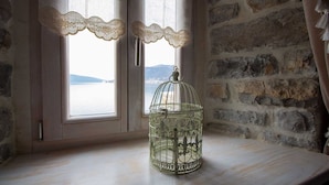 A birdcage on a wooden table by a window with lace curtains, overlooking a body of water and mountains. - Villa Stella Adriatica (Tivat)